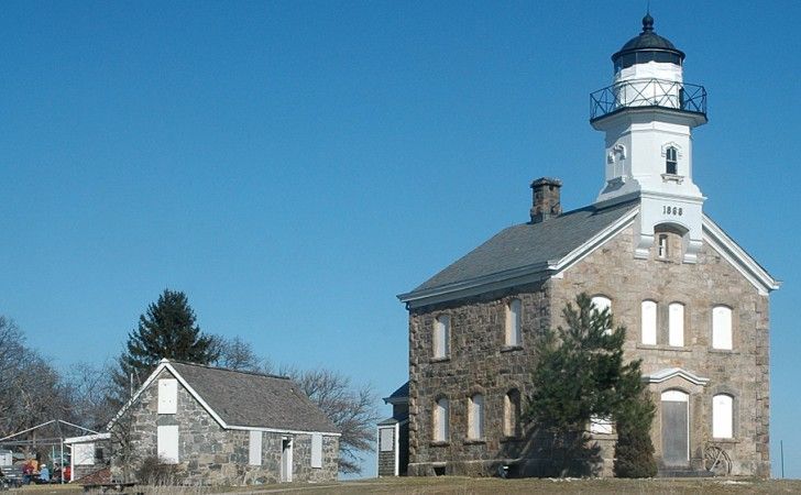 A stone lighthouse and an adjacent stone outbuilding under a clear blue sky.
