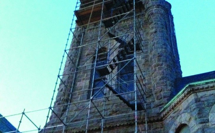 A stone clock tower under construction with metal scaffolding surrounding the exterior.