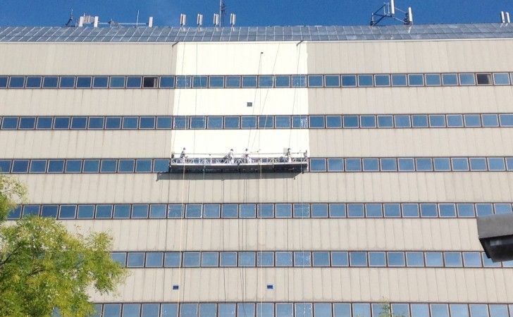 A suspended platform with two workers performing maintenance on the exterior facade of a large office building.