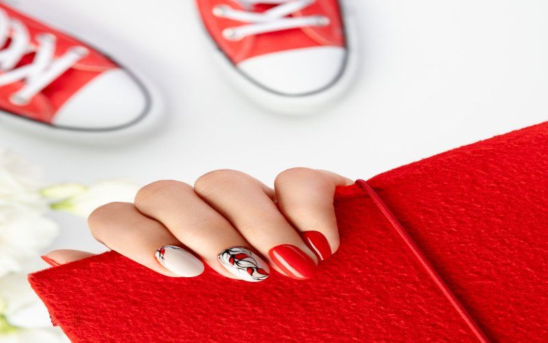 Una mano con nail art rossa e argento appoggiata su una pochette rossa.