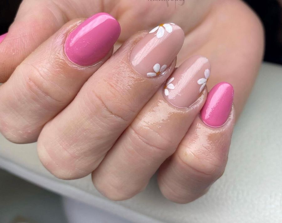 Mano con manicure rosa e unghie nude trasparenti con piccoli dettagli floreali bianchi.