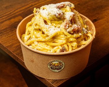 Pasta cremosa condita con formaggio grattugiato, pepe nero e pezzetti di pomodoro su un piatto bianco.
