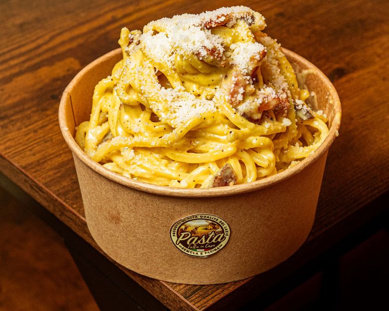 Piatto di spaghetti alla carbonara con pancetta e formaggio grattugiato su un piatto scuro.