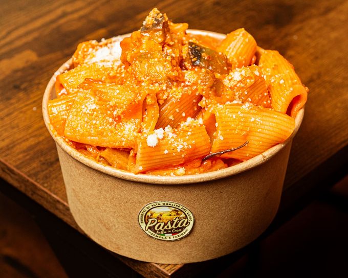 Una ciotola di rigatoni al sugo di pomodoro con polpette su un tavolo di legno.