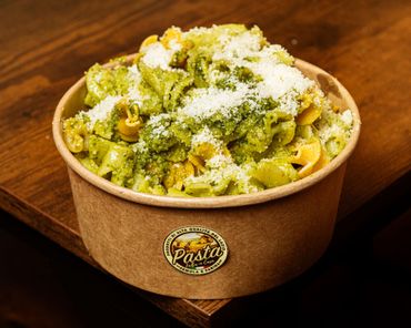 Piatto di pasta al pesto verde su un tavolo rustico, guarnito con foglie di basilico.