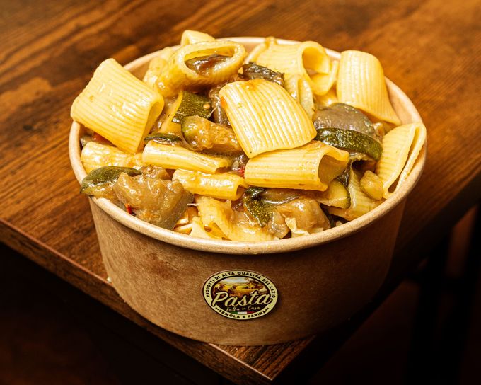 Ciotola di rigatoni con verdure e sugo su un tavolo di legno.