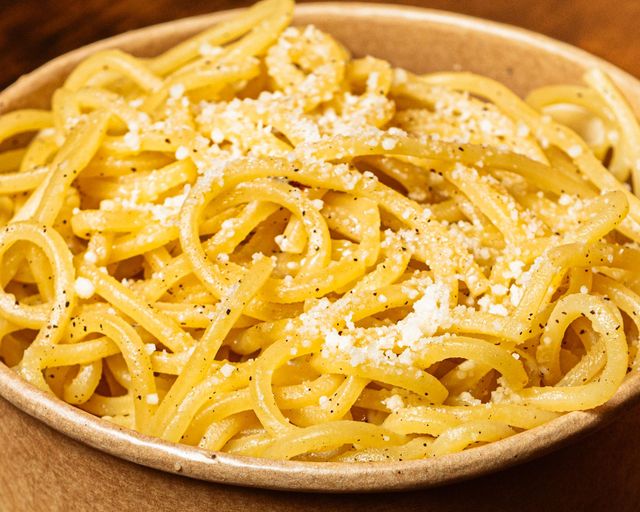 Piatto di spaghetti conditi con formaggio grattugiato su un tavolo di legno.