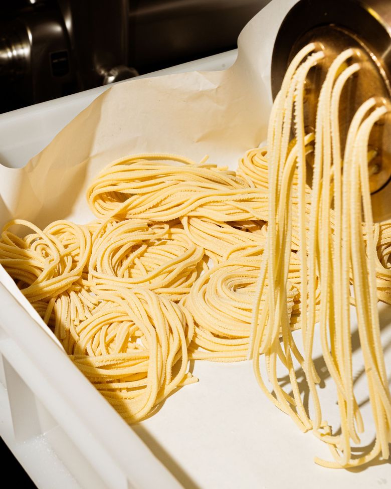 Pasta fresca estrusa da una macchina in un vassoio bianco.