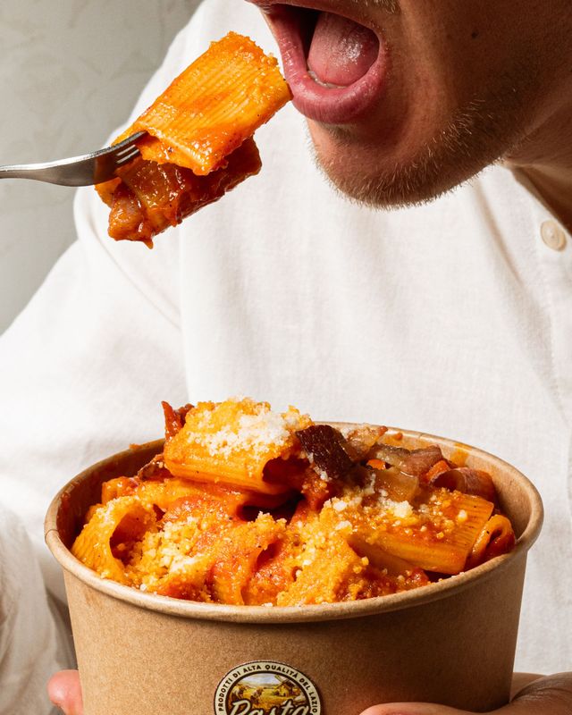 Persona che mangia pasta con salsa all'arancia da una ciotola da asporto con la forchetta
