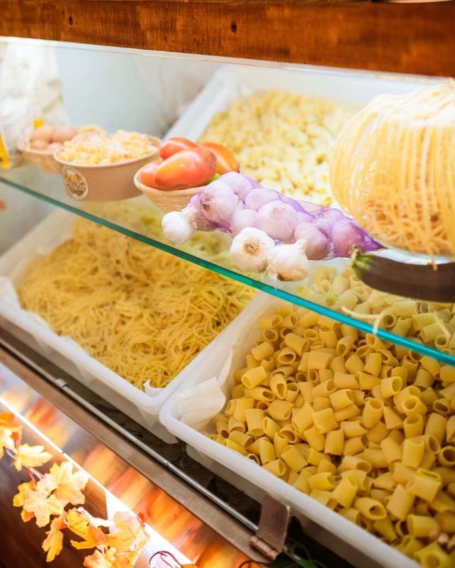Vetrina da forno in vetro con vassoi di pasta assortita nei toni del giallo, del viola e del beige.