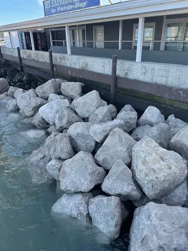Large, gray riprap rocks line a waterfront seawall near a building marked with a 