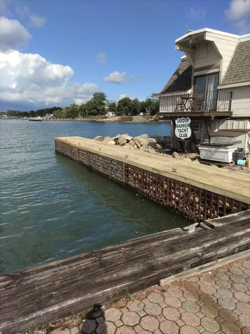 A stone pier extending into a calm lake next to a wooden building under a partly cloudy blue sky.