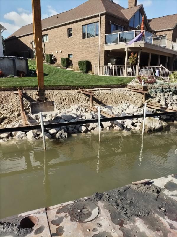 Construction equipment excavating a residential shoreline bank along a water channel.