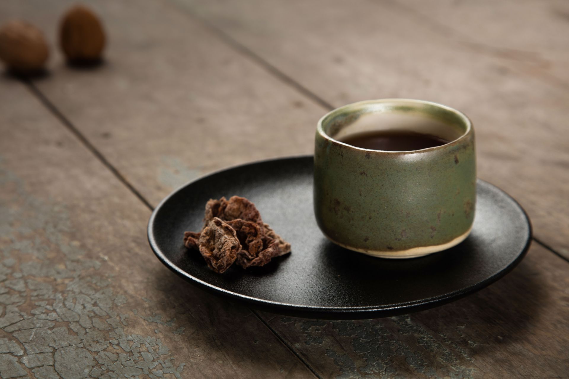 木桌上,黑色盤子裡盛著一杯茶,旁邊放著黑巧克力。