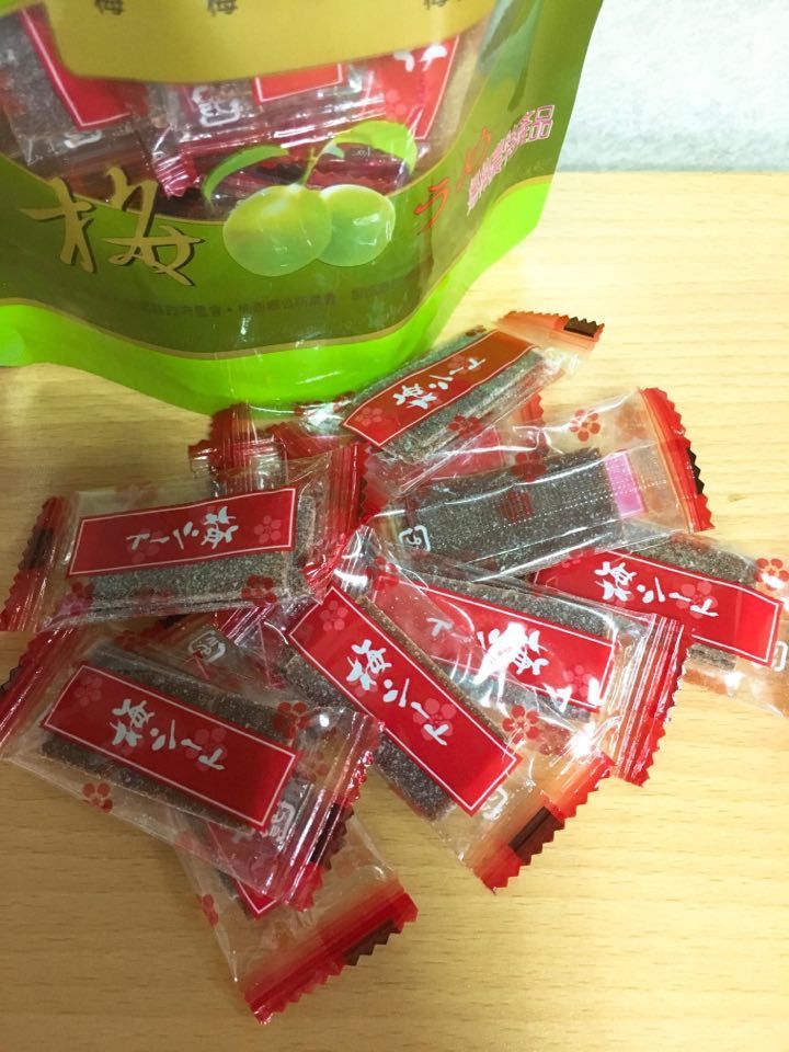 獨立包裝的梅子糖從一個半露在外的綠色袋子裡傾瀉而出,袋子放在木質表面上。