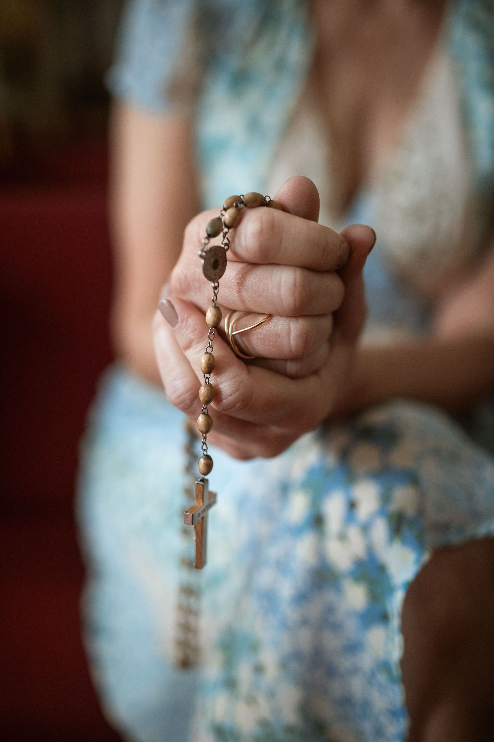 Hands holding a rosary with a cross pendant against a blurred background, suggesting prayer or reflection