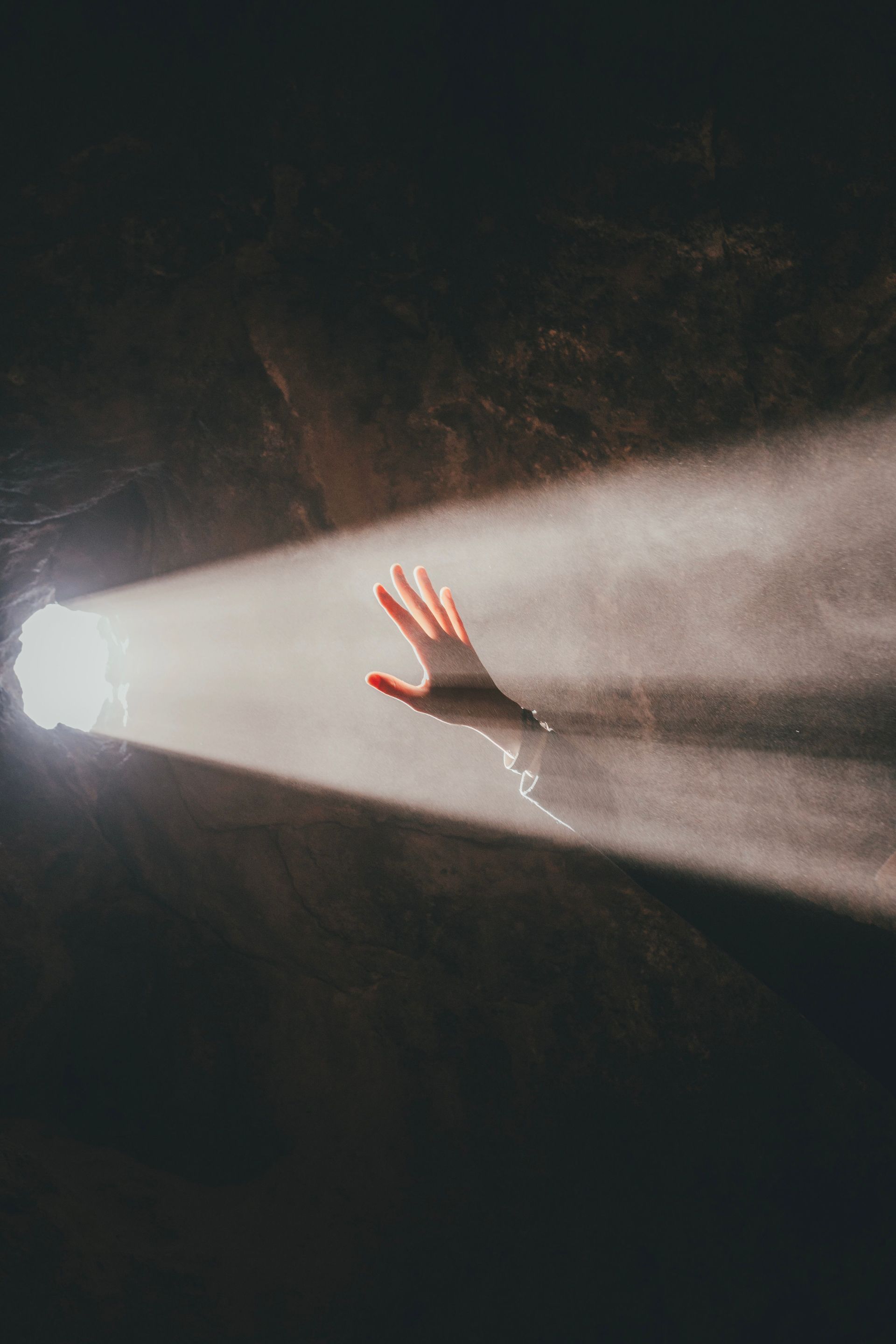 Hand reaching into a bright beam of light in a dark, smoky scene