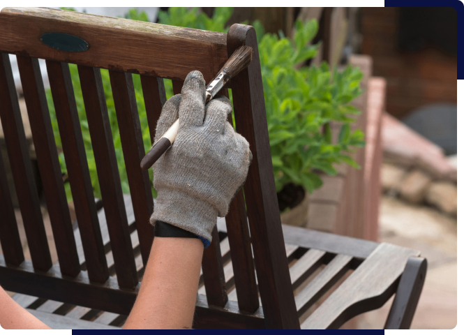 Person wearing glove painting wooden bench outdoors.