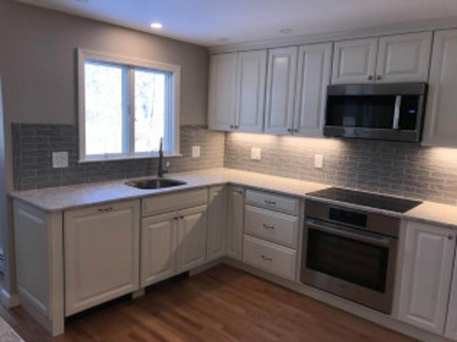 White kitchen with cabinets, stainless steel appliances, and gray backsplash.