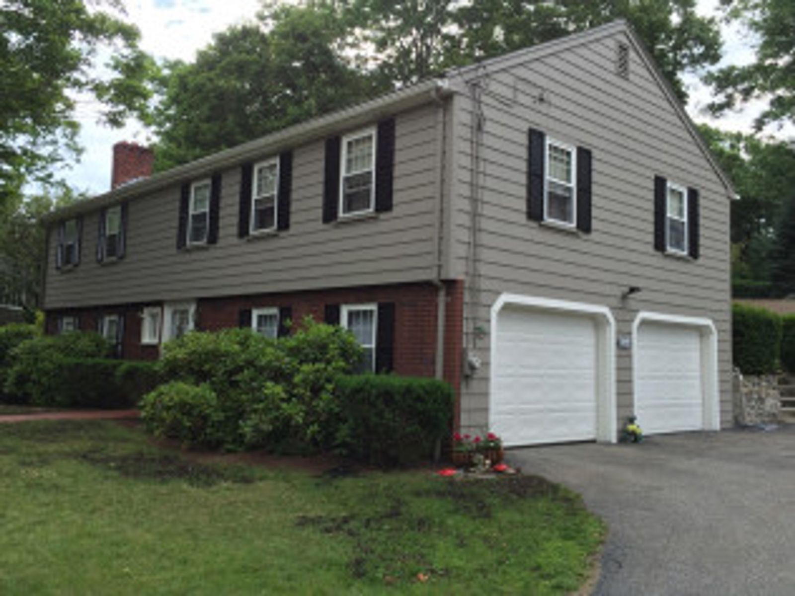 Two-story house with gray siding, red brick, and a two-car garage. Black shutters and a front lawn.