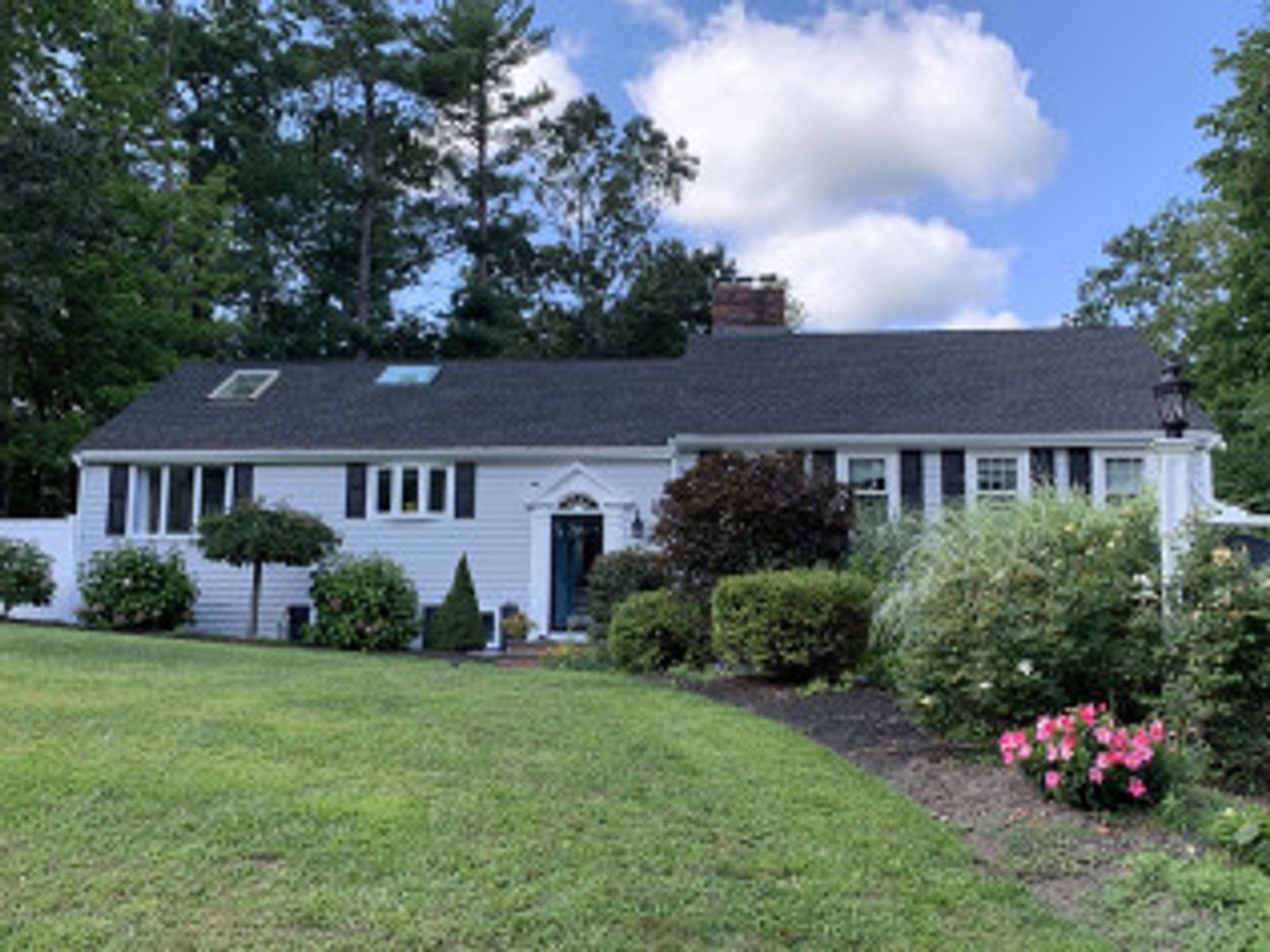 White ranch house with black shutters, green lawn, and blue sky.
