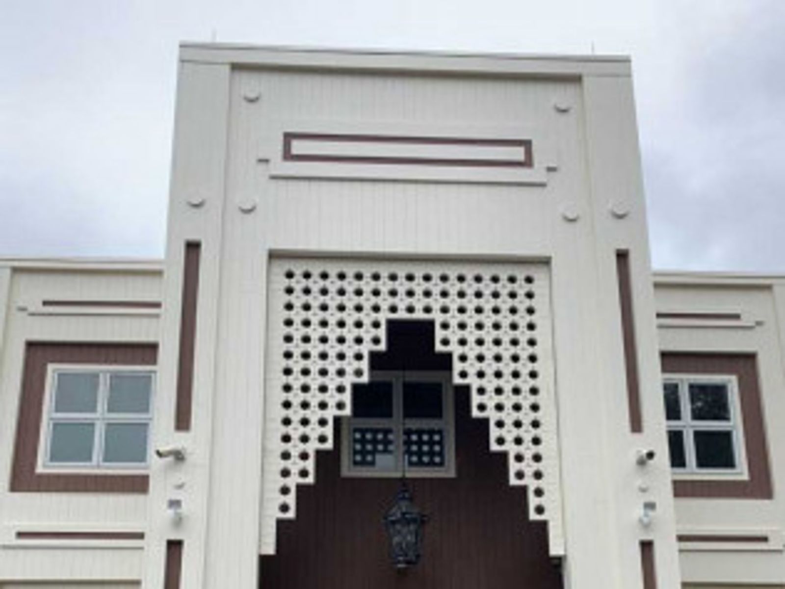White building with brown trim, decorative openwork, and windows under an overcast sky.