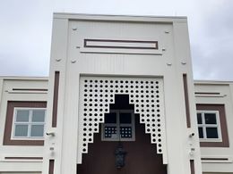 White building facade with decorative cutouts and windows against a cloudy sky.