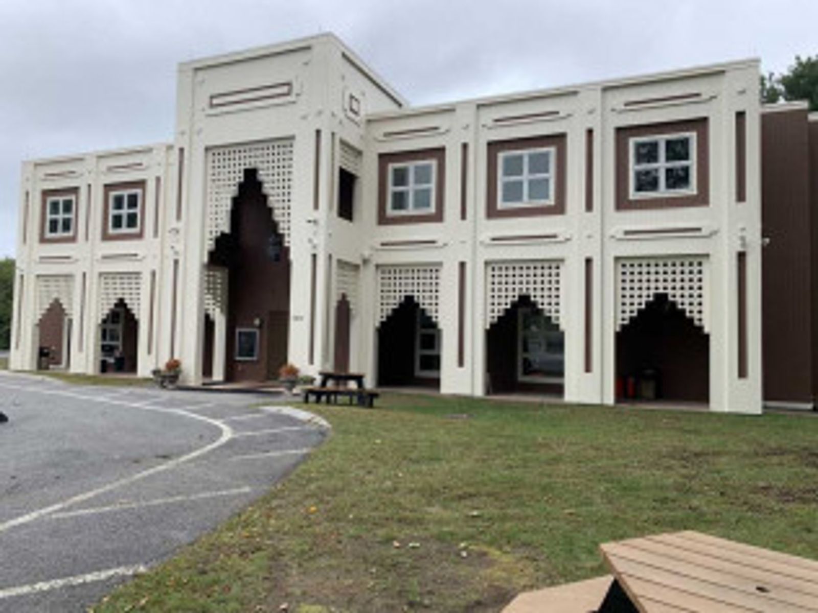 Beige and brown building with arched entryways and square windows, a picnic table on the lawn.