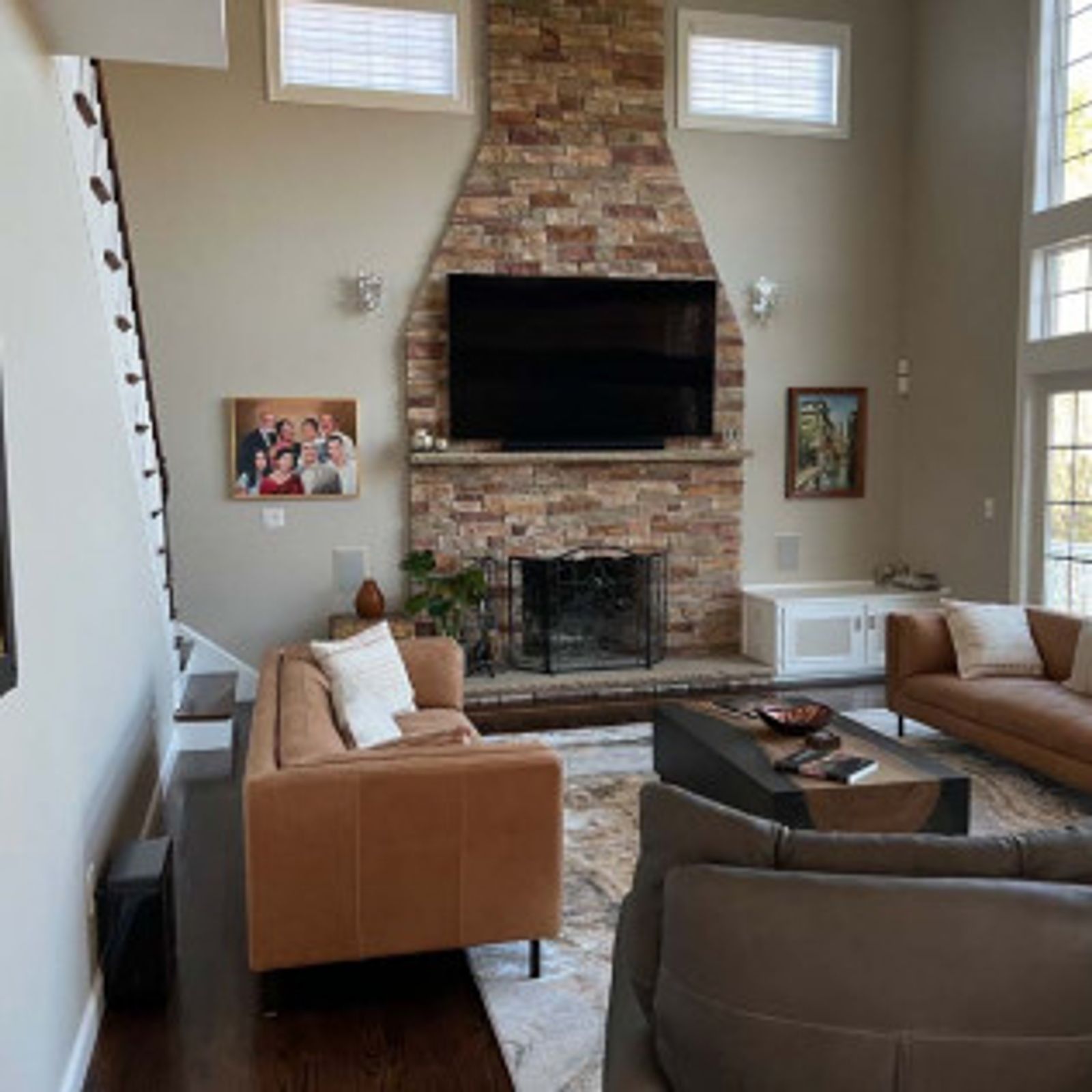 Living room with stone fireplace, TV, brown leather sofas, and area rug.