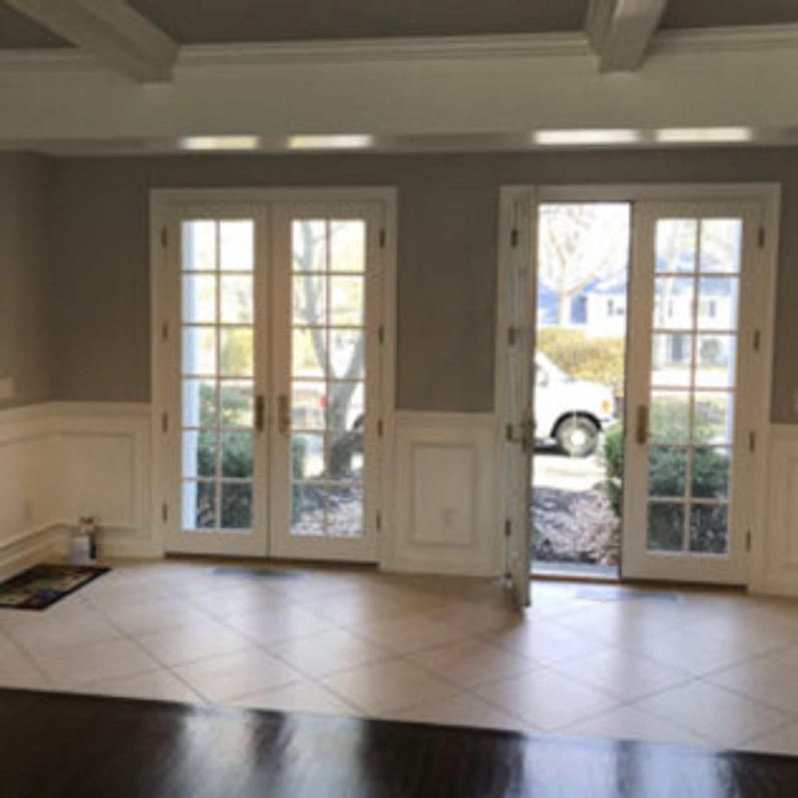 Interior view: French doors, tan tiled floor, white trim, grey walls, partial view of street.