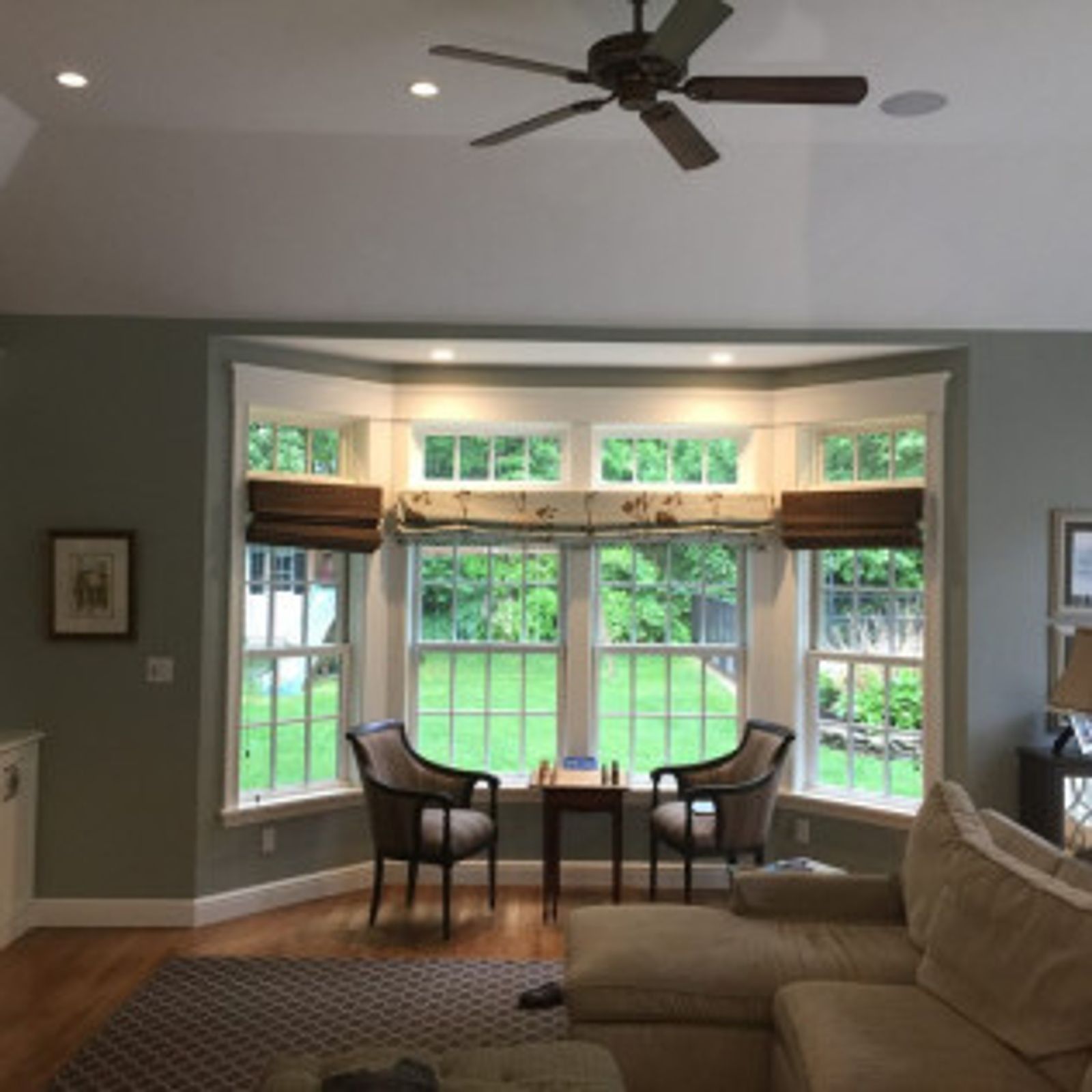 Living room with bay window, two chairs, table. Green walls, wood floors, brown and white window treatments.