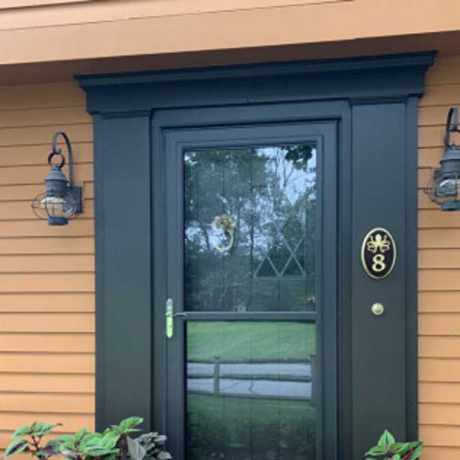 Black door with sidelights, address plaque, and lanterns, set against a tan house exterior.