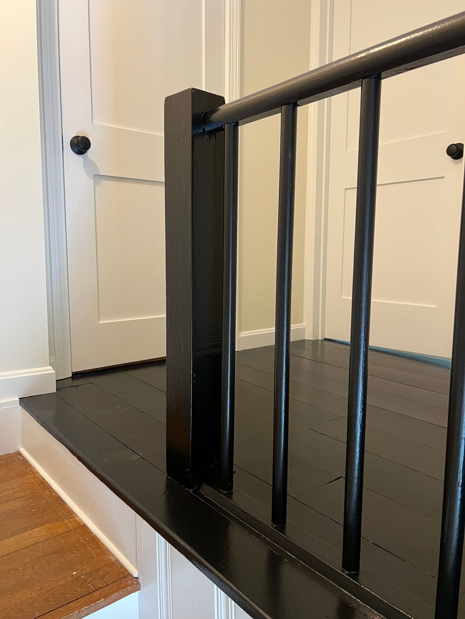 Black stair railing and newel post on a black platform, white door in the background.