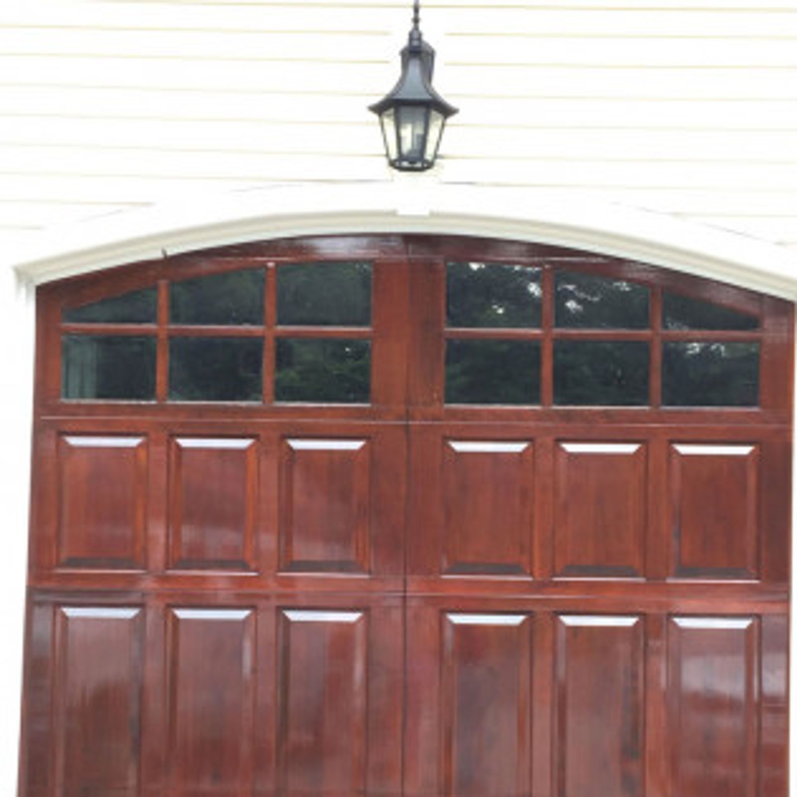 Dark wood garage door with arched top and glass windows. Black outdoor light above.