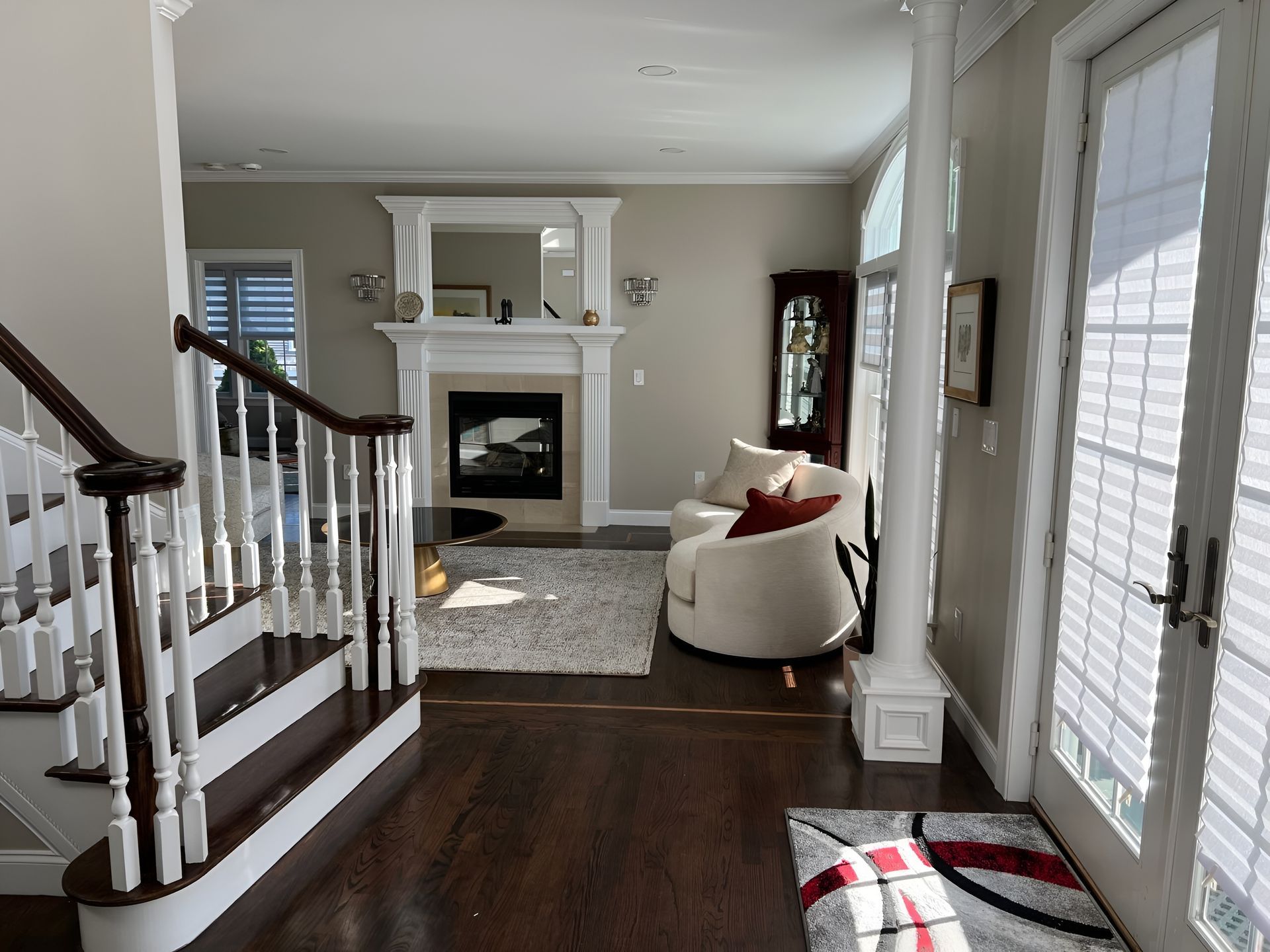 Interior view: living room with fireplace, stairs, armchair, rug, and doorway with sunlight.
