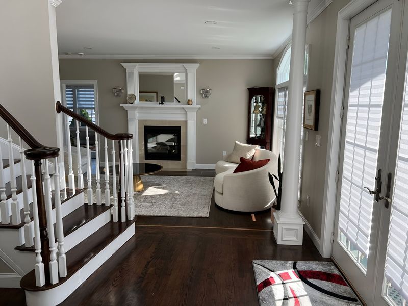 Interior view: living room with fireplace, stairs, armchair, rug, and doorway with sunlight.