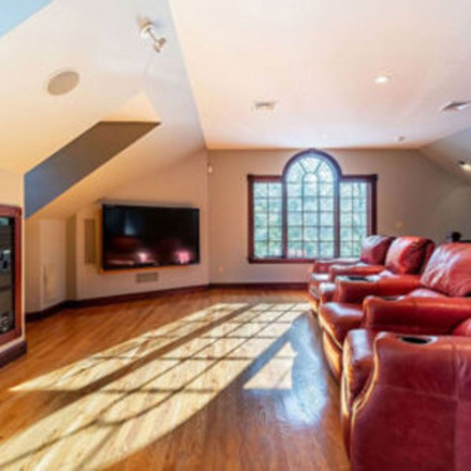 Home theater with red leather recliners, large TV, hardwood floor, arched window.