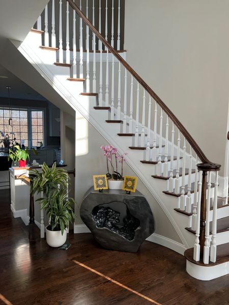 Staircase with white spindles, brown railing, and dark hardwood floors. A dark stone-like console table sits below.