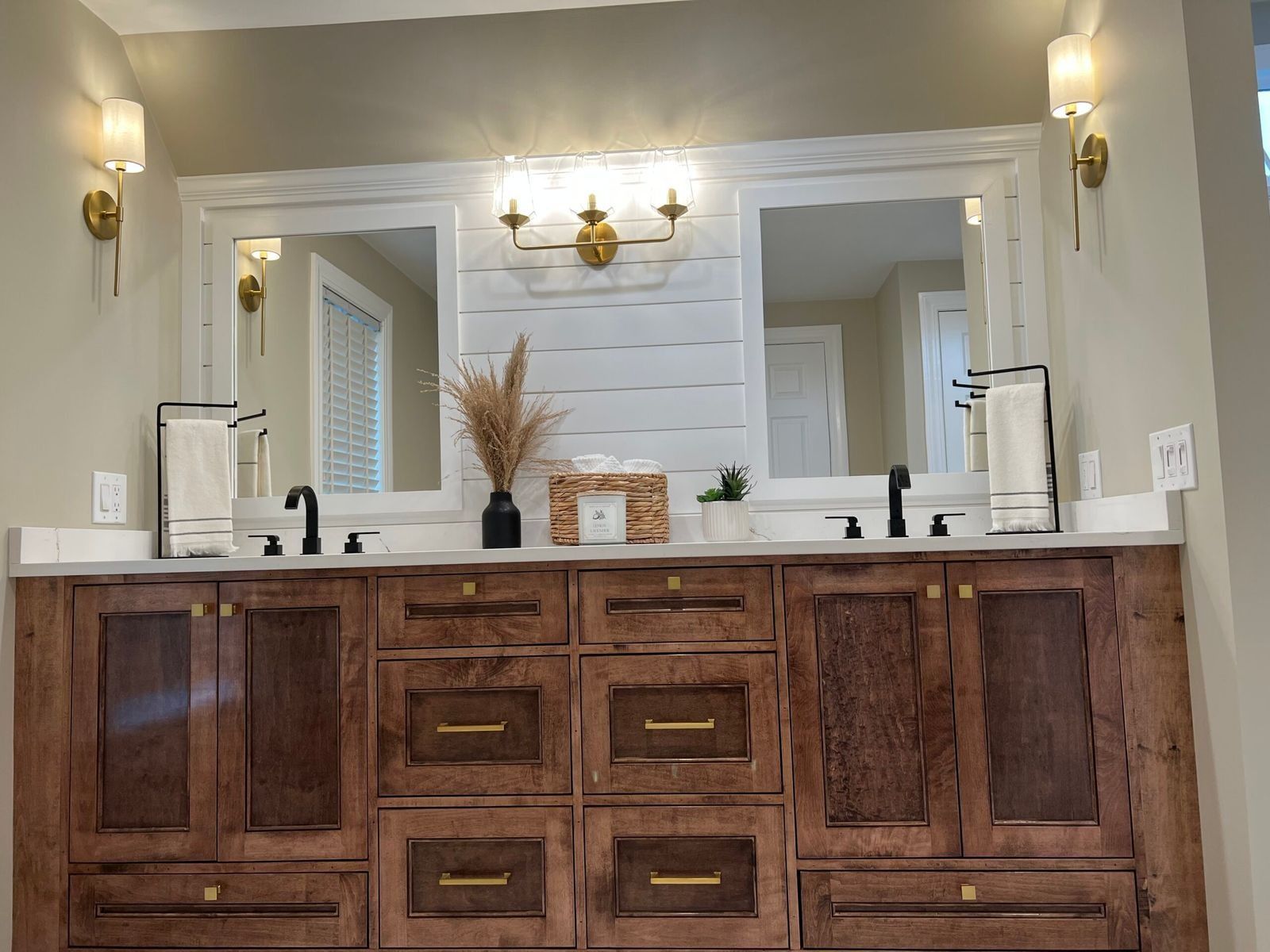 Bathroom vanity with two mirrors, wood cabinets, white countertop, and gold light fixtures.