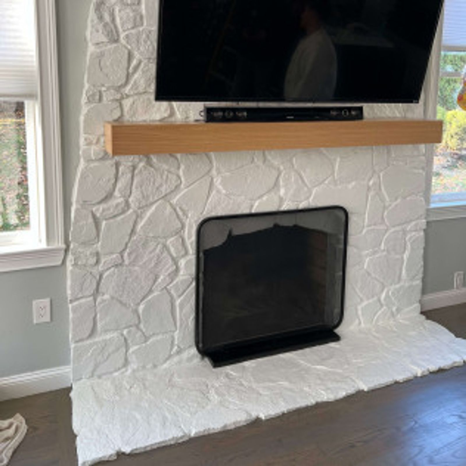 White stone fireplace with a black TV, soundbar, and wooden mantle.