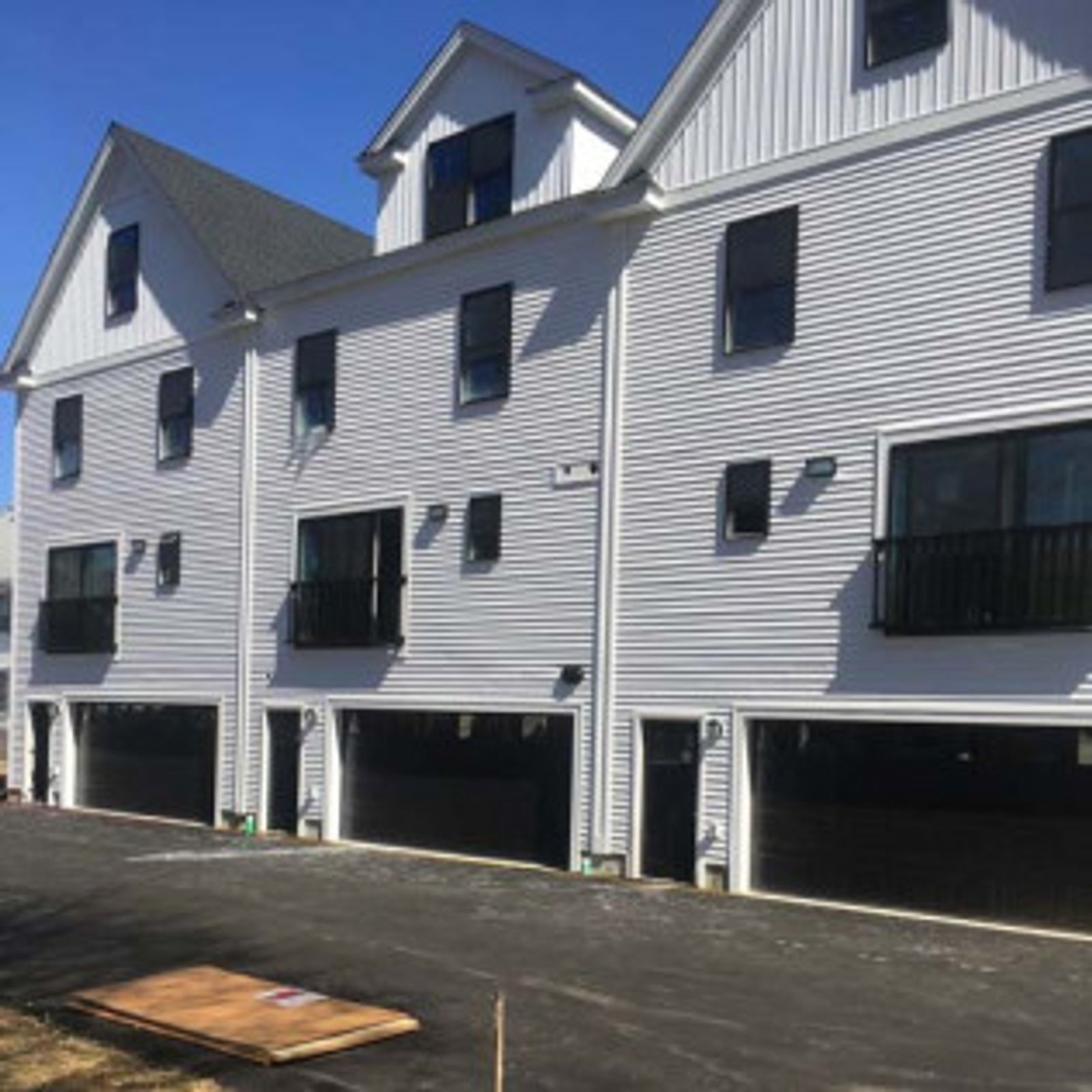 Row of modern white townhouses with black garages and windows under a blue sky.