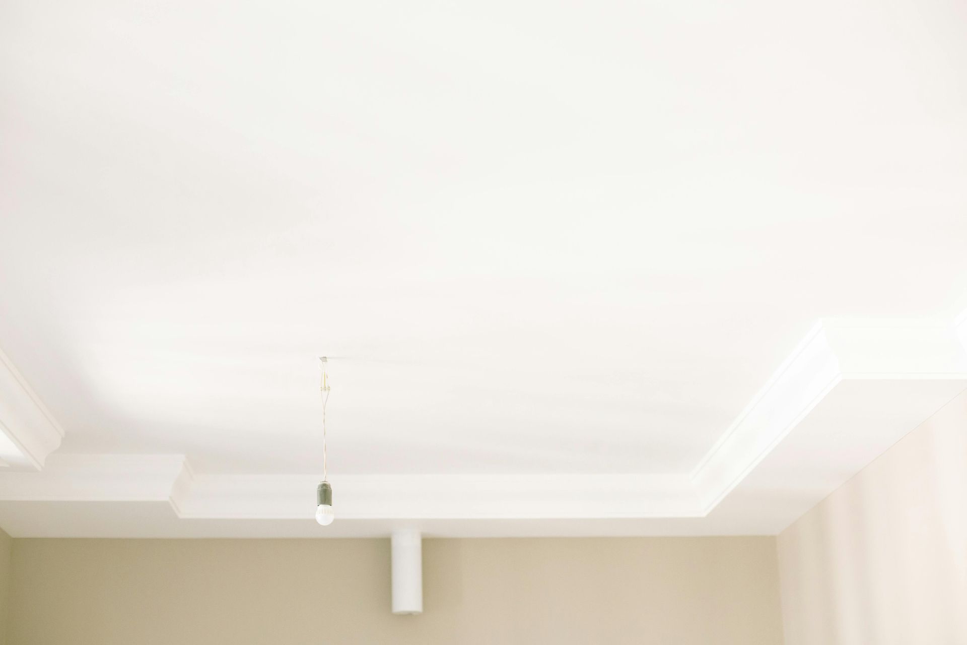 White ceiling with a recessed border and a hanging light fixture. Beige walls below.