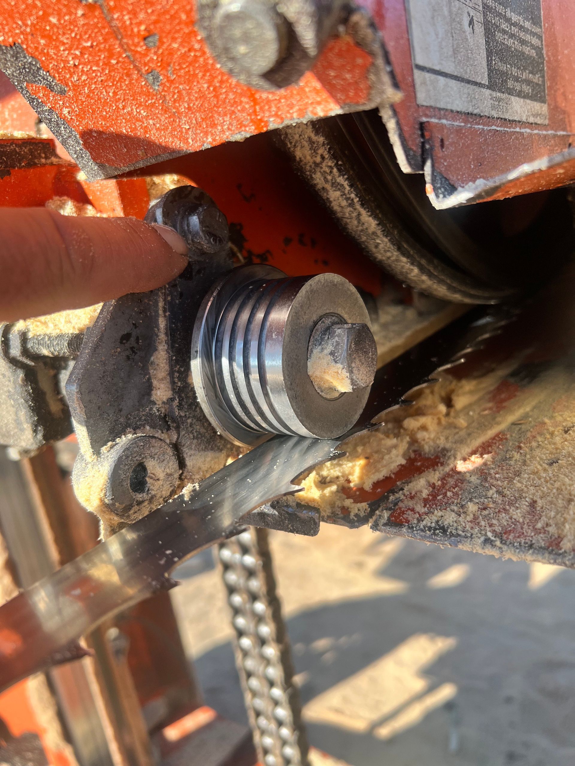Close-up of a saw blade guide assembly on a sawmill, showing a metal guide wheel next to a moving blade.