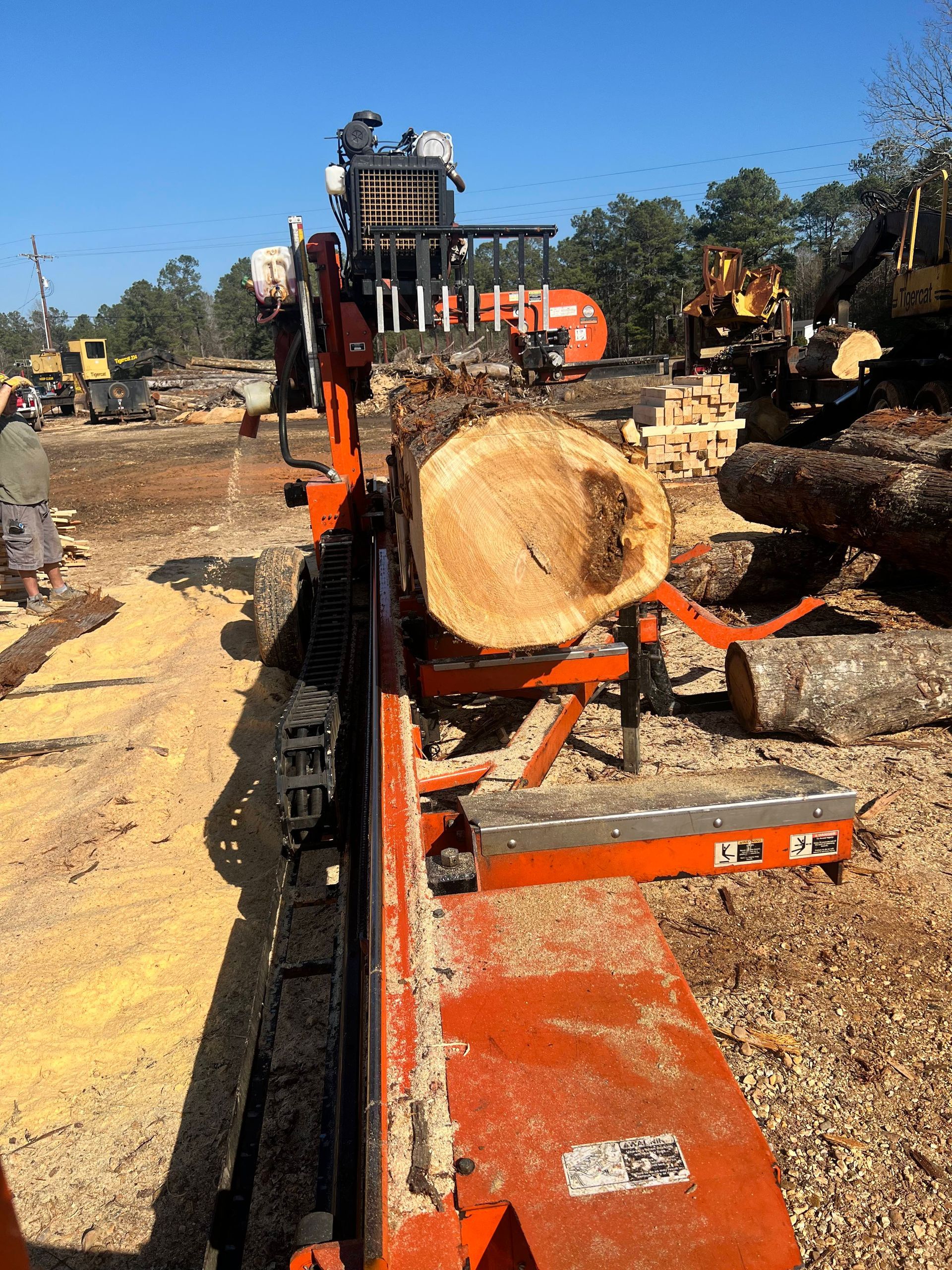 A lumber mill with a large log being cut by an orange saw, operator visible.