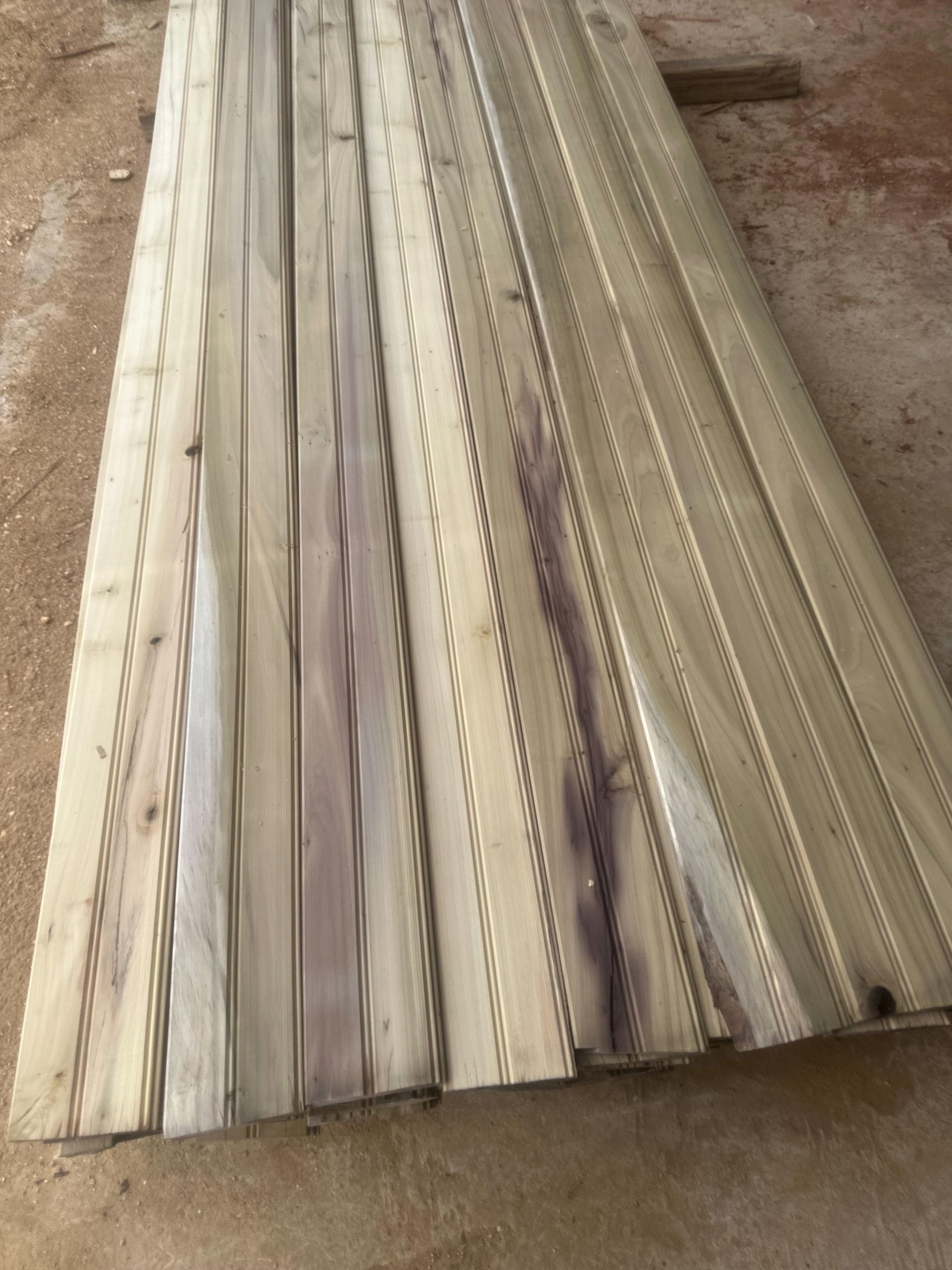 Wooden planks stacked, some with grooved patterns, outdoors.