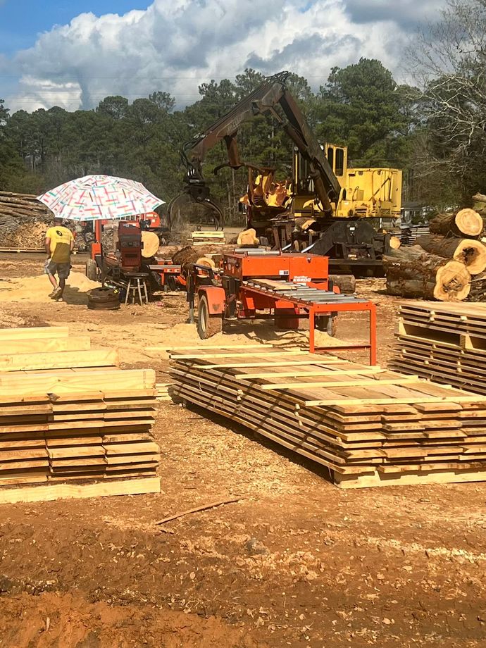 Lumber mill with stacks of wood, machinery, and a person under a sun umbrella.