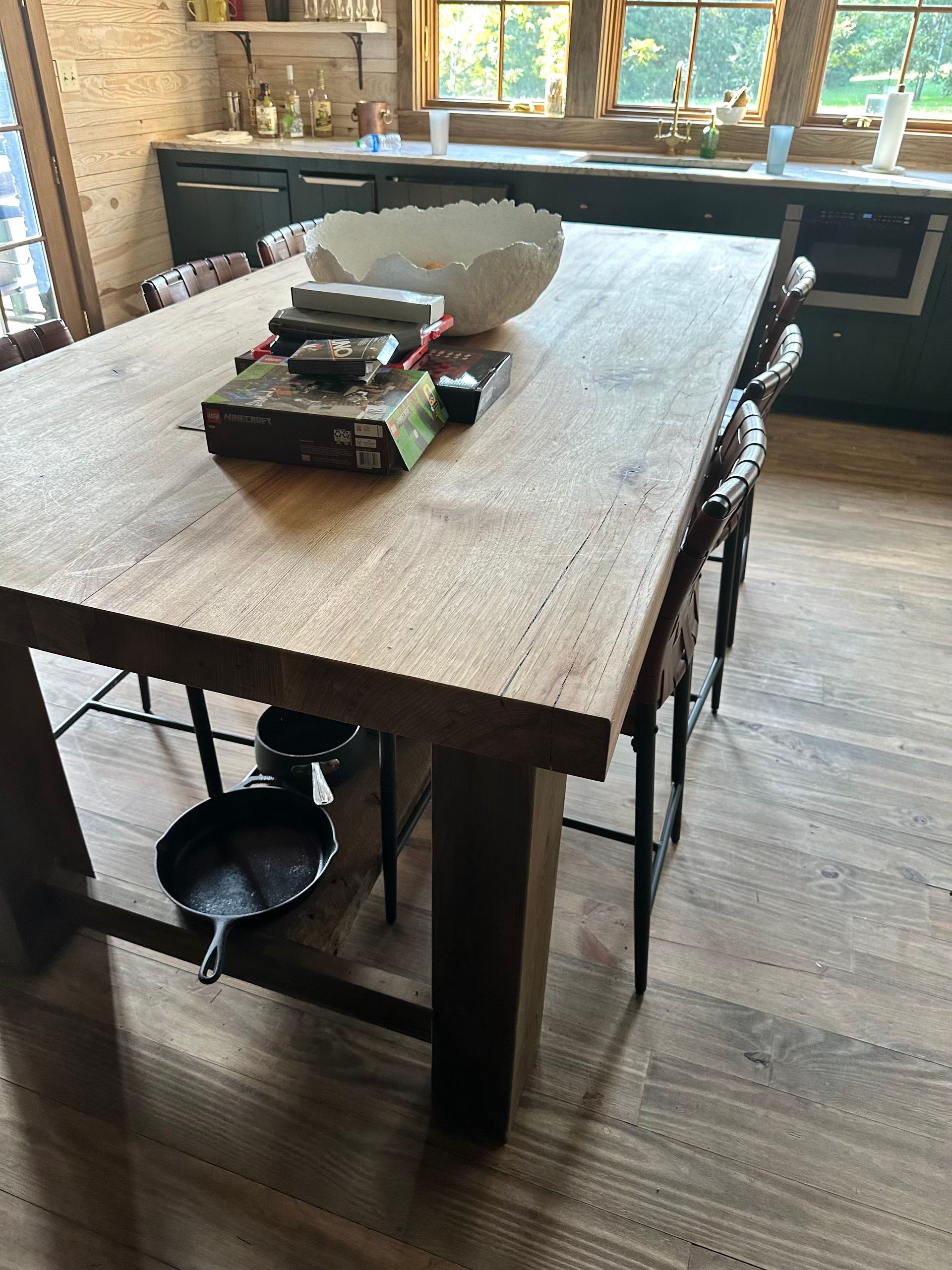 Wooden kitchen table with cast iron pan, bowl, and game. Dark cabinets and window in the background.