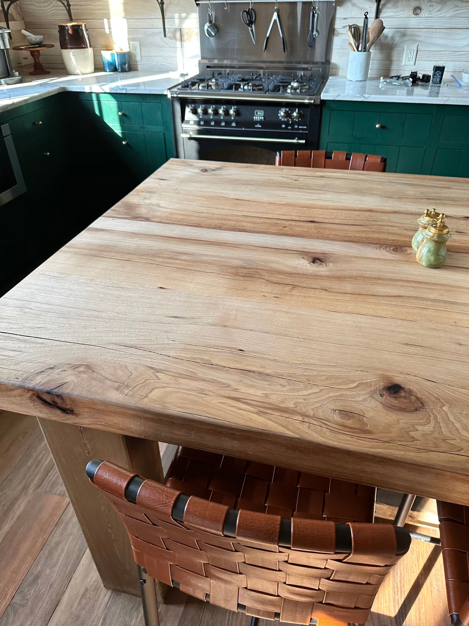 Wooden table in a kitchen with a green cabinet and a stainless steel stove. A woven leather chair sits near the table.