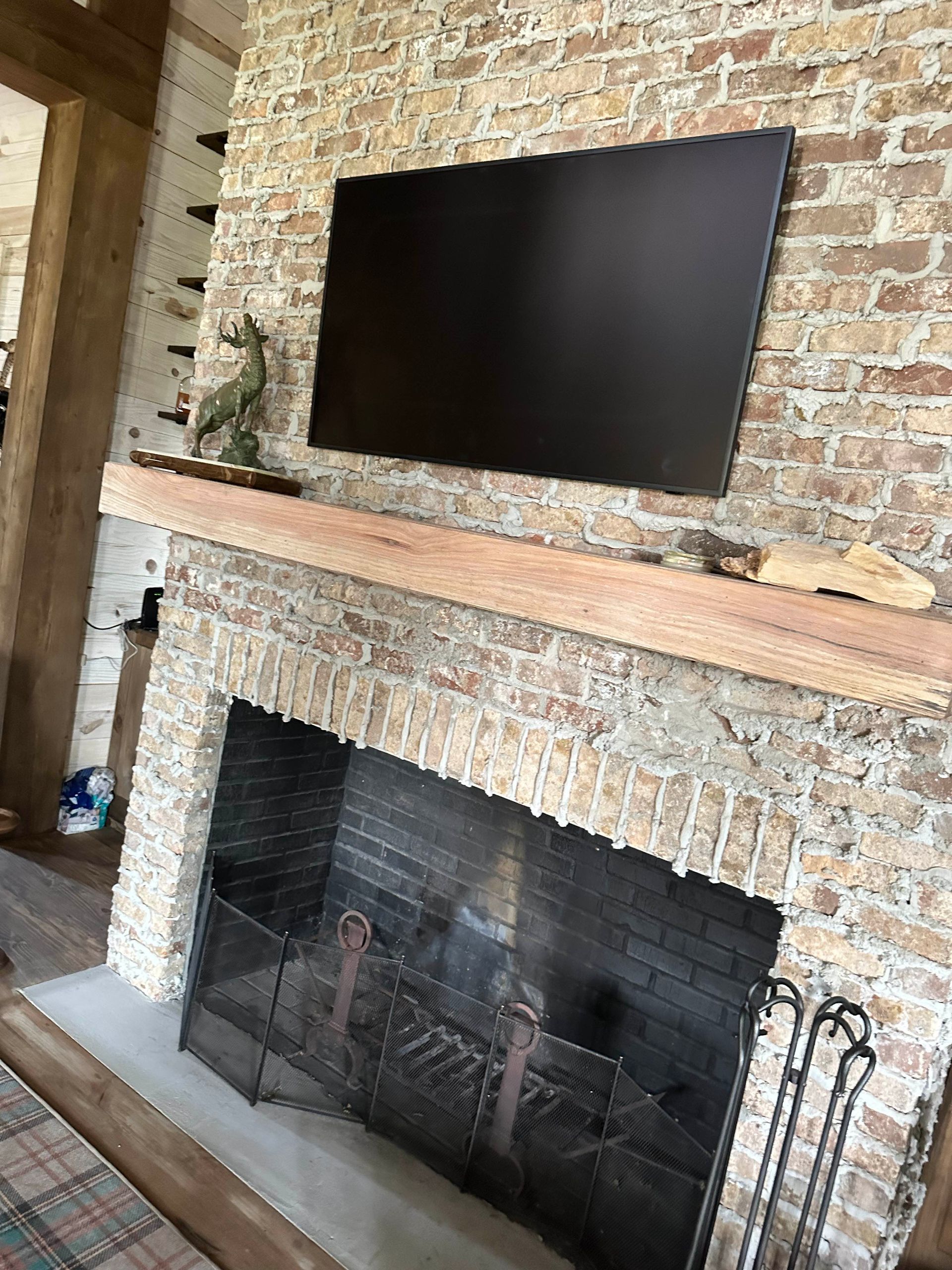 Brick fireplace with a mounted television. Fireplace has a metal screen, wooden mantle.