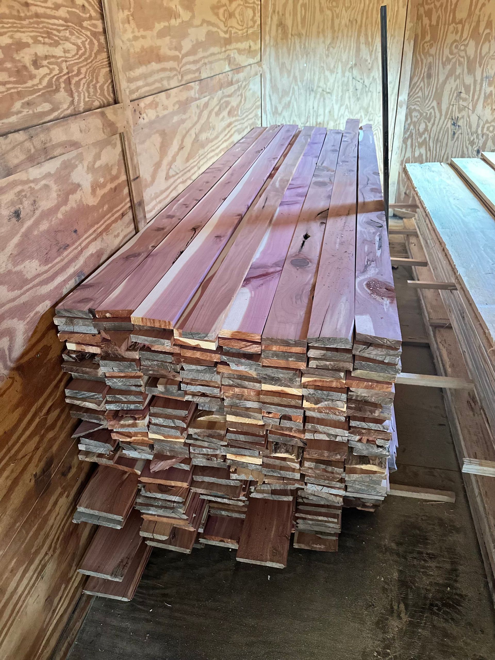 Stack of reddish-brown cedar wood planks in a wood-lined storage space.